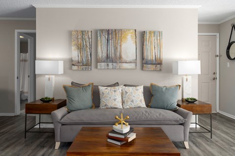 A living room with a grey couch, a coffee table, and three paintings on the wall.